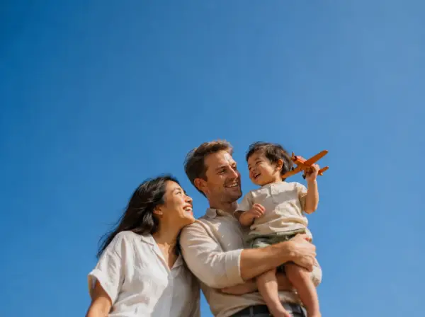 A mother and father with their toddler, who is holding up a toy plane, under a blue sky